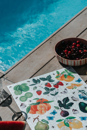 Fruit-themed placemat on a wooden deck by a pool