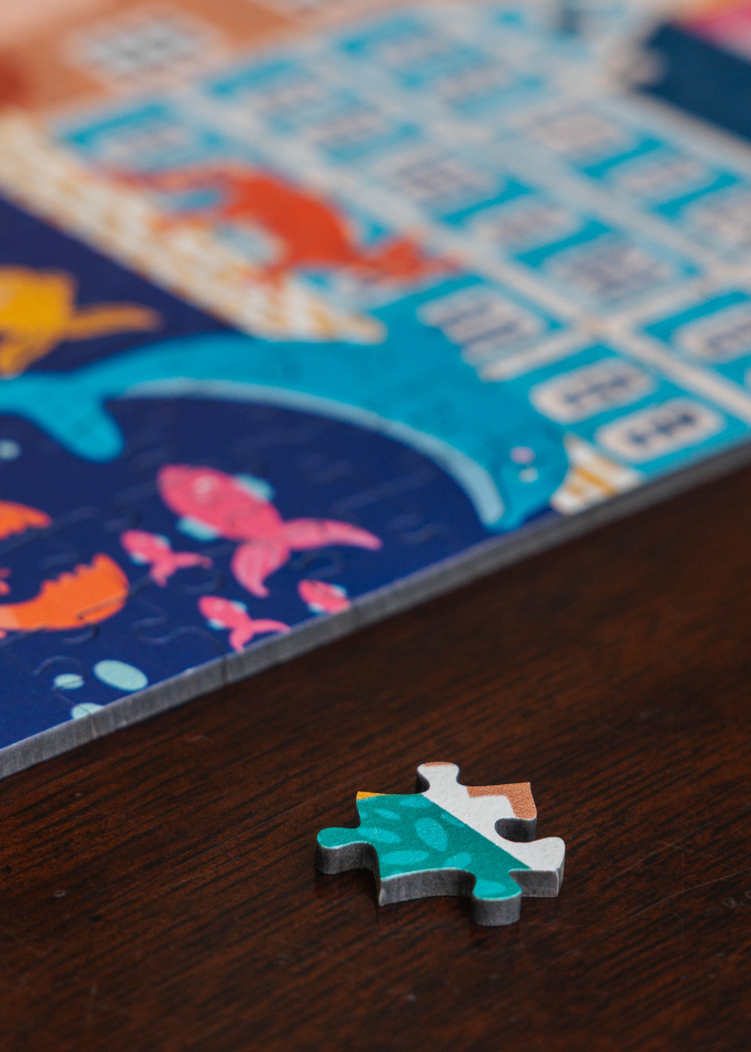 Close-up of a partially completed puzzle on a wooden surface with a colorful puzzle piece in focus. Cape Town by Kelly McChesney