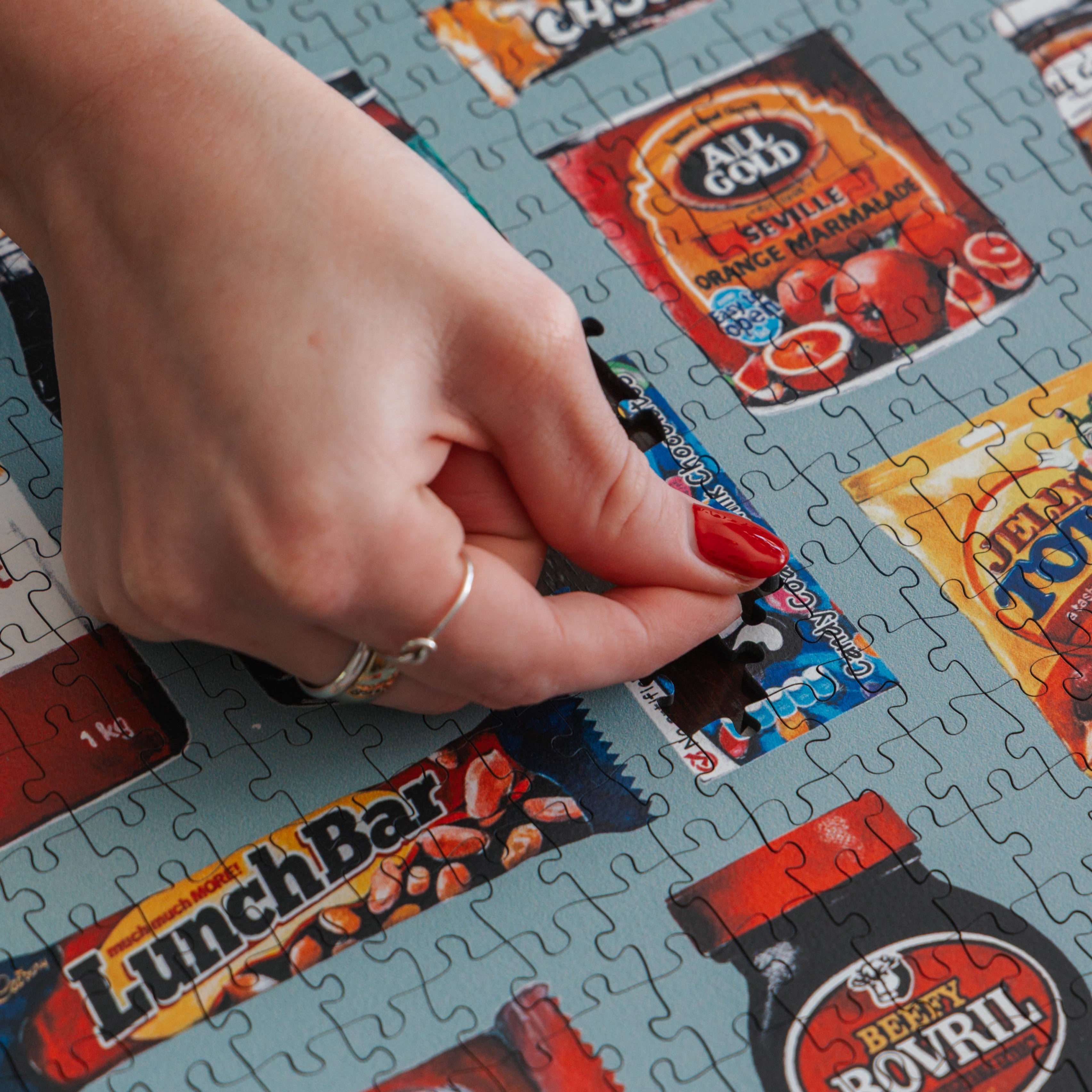 Hand placing a puzzle piece on a tray with retro food packaging designs. masterpiece puzzles. wooden puzzle. south africa. 