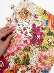 Floral puzzle with a hand placing a piece, featuring vibrant flowers and leaves.