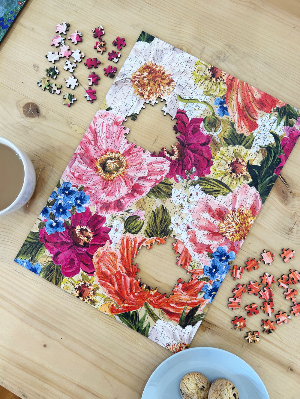 Floral puzzle on a wooden table with scattered pieces and a cup.