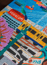 Colorful puzzle with Vodacom and FNB branding, held by a hand. Johannesburg by Kelly McChesney Puzzle