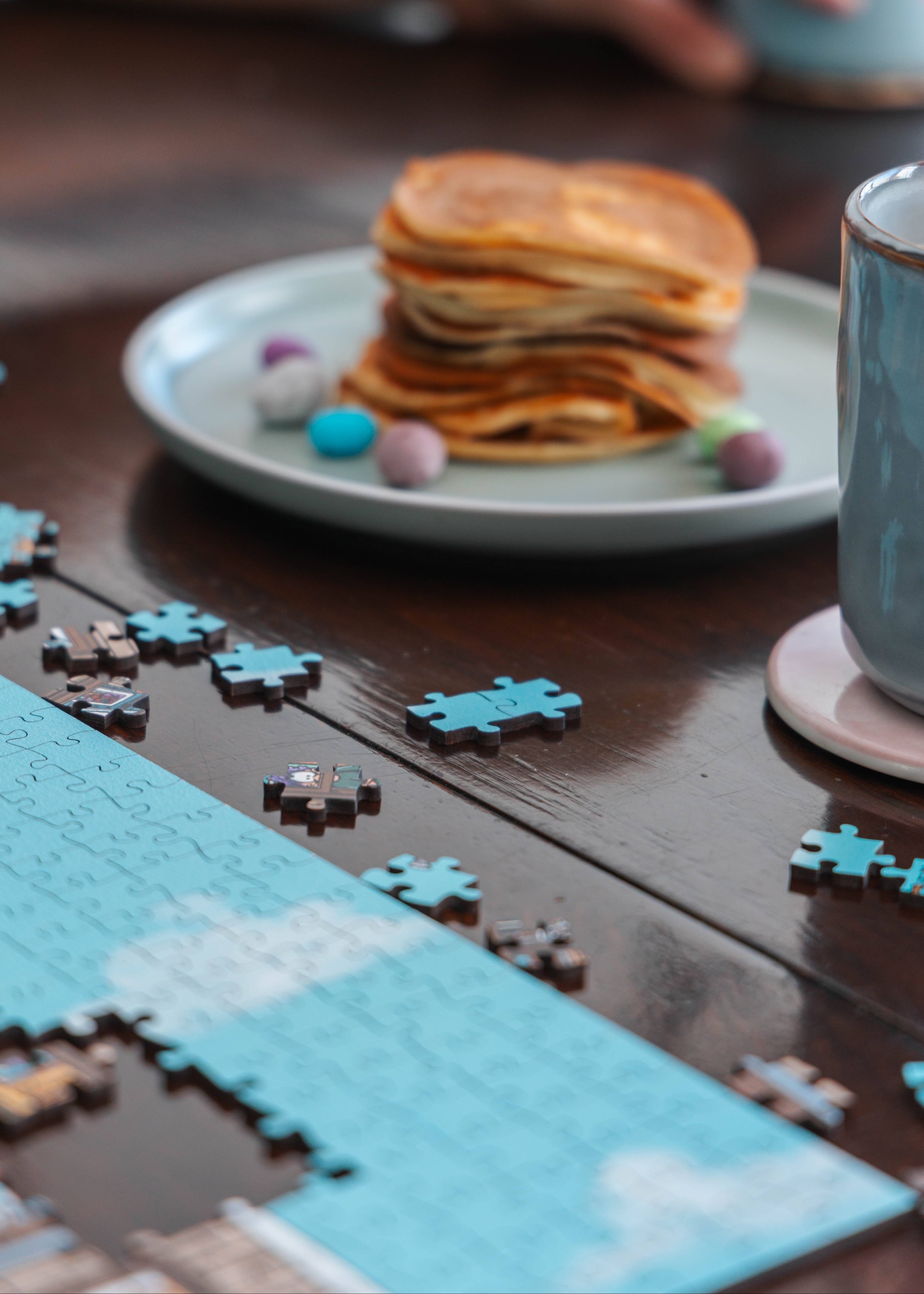 Pancakes with syrup, colorful candies, and a wooden puzzle on a wooden table.