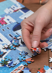 Hand placing a puzzle piece on a Santorini-themed puzzle