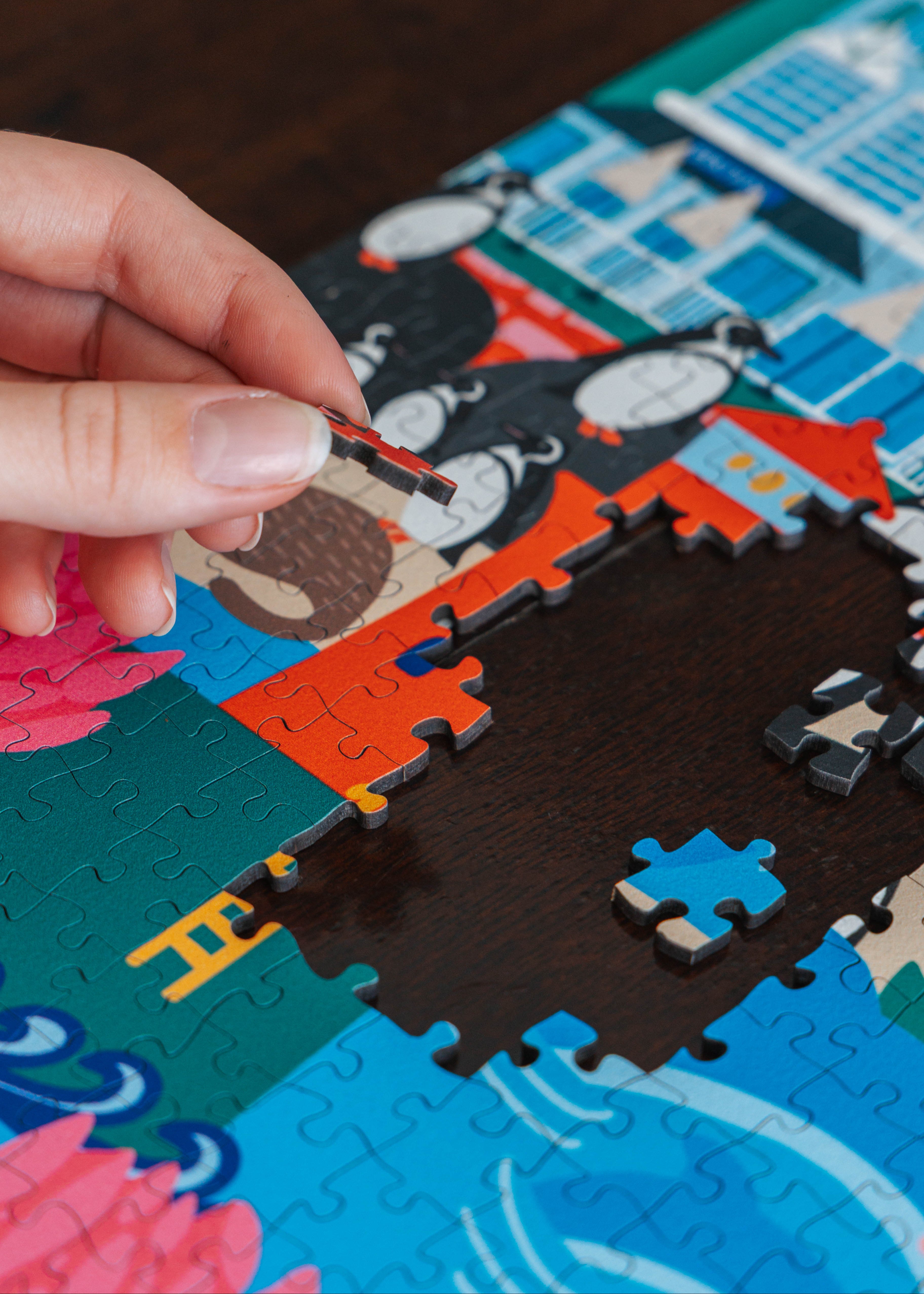 Hand completing a puzzle piece on a colorful puzzle mat with a boat design. Simon's Town Penguins