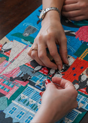 Two hands working on a colorful puzzle with cartoon characters. Simon's Town Penguins