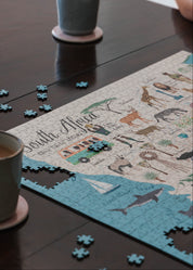 Jigsaw puzzle of South Africa on a table with coffee cups and puzzle pieces.
