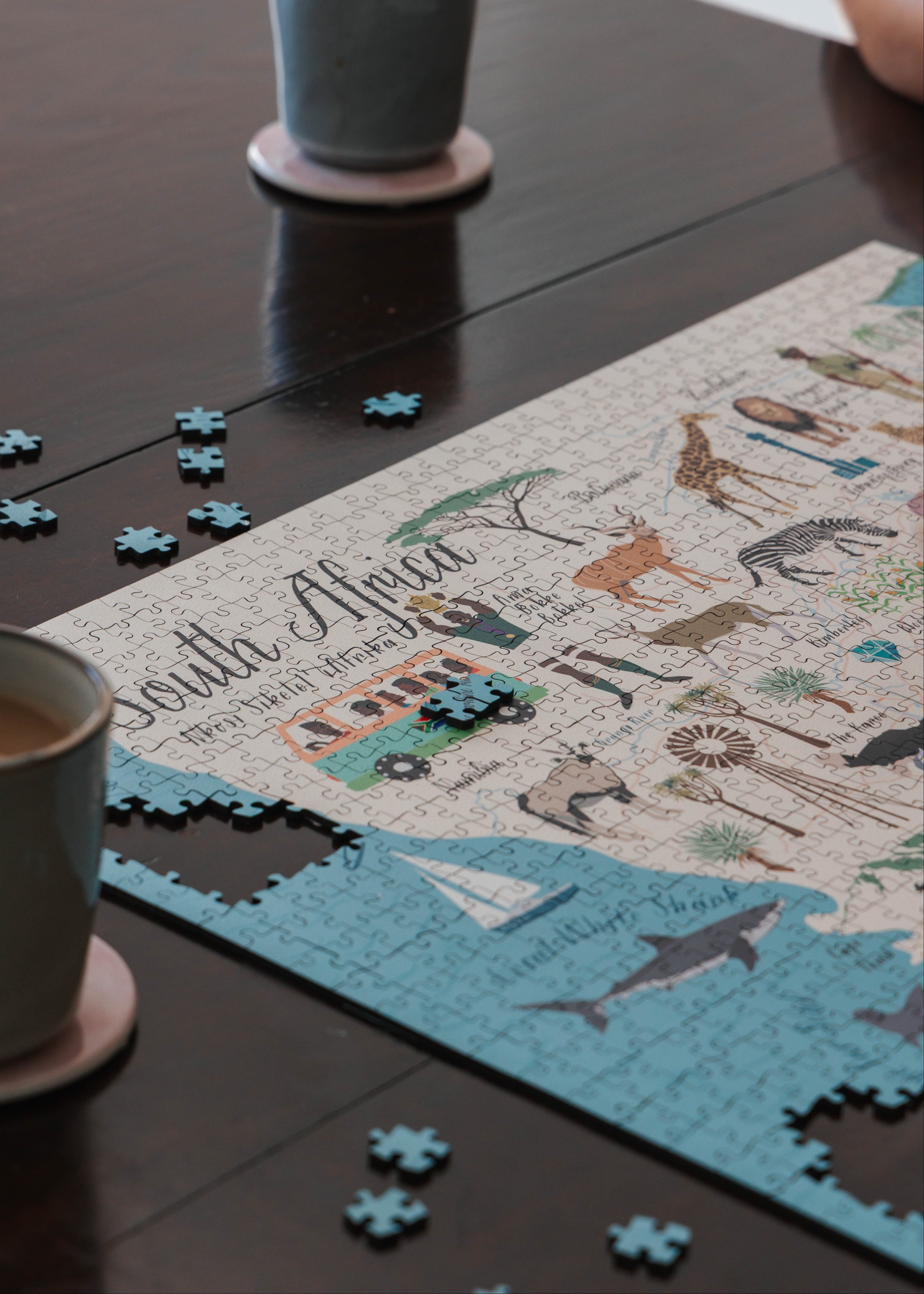 Jigsaw puzzle of South Africa on a table with coffee cups and puzzle pieces.