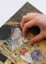 The Kiss is a MasterPiece wooden jigsaw puzzle of one of Gustav Klimt’s most celebrated paintings. This artwork of the Golden Period portrays an intimate embrace between two lovers, enveloped in a shimmering golden cloak adorned with intricate patterns. 

Precision-cut from 3mm thick wood and expertly printed, our MasterPiece puzzles offer a tactile and satisfying puzzling experience like no other. They are perfect for classic art lovers and anyone looking for a thoughtful gift. 