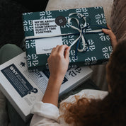 Person holding a wrapped gift with a visible brand logo on a couch.