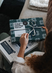 Person holding a wrapped gift with a visible brand logo on a couch.