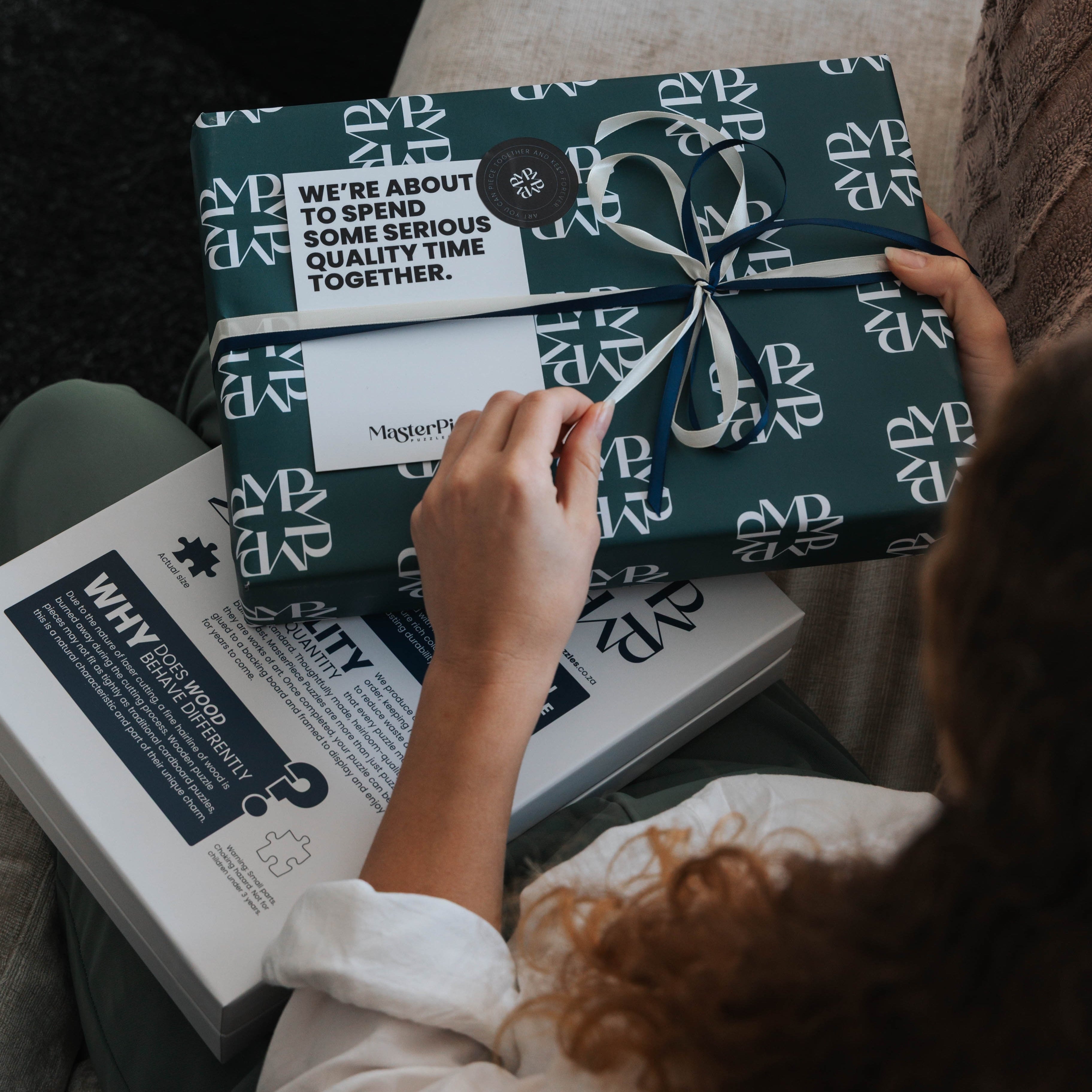 Person holding a wrapped gift with a visible brand logo on a couch.