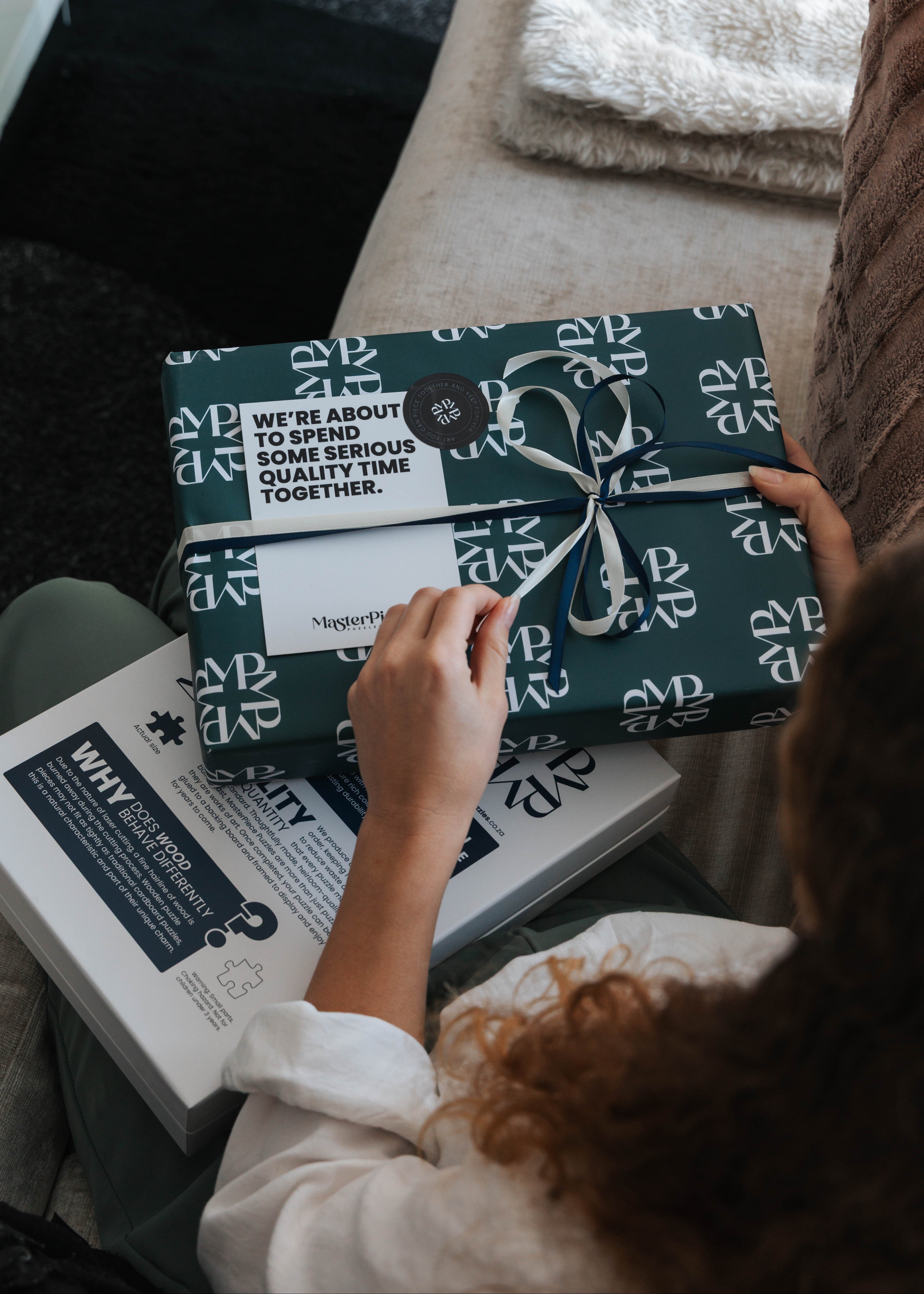 Person holding a wrapped gift with a visible brand logo on a couch.