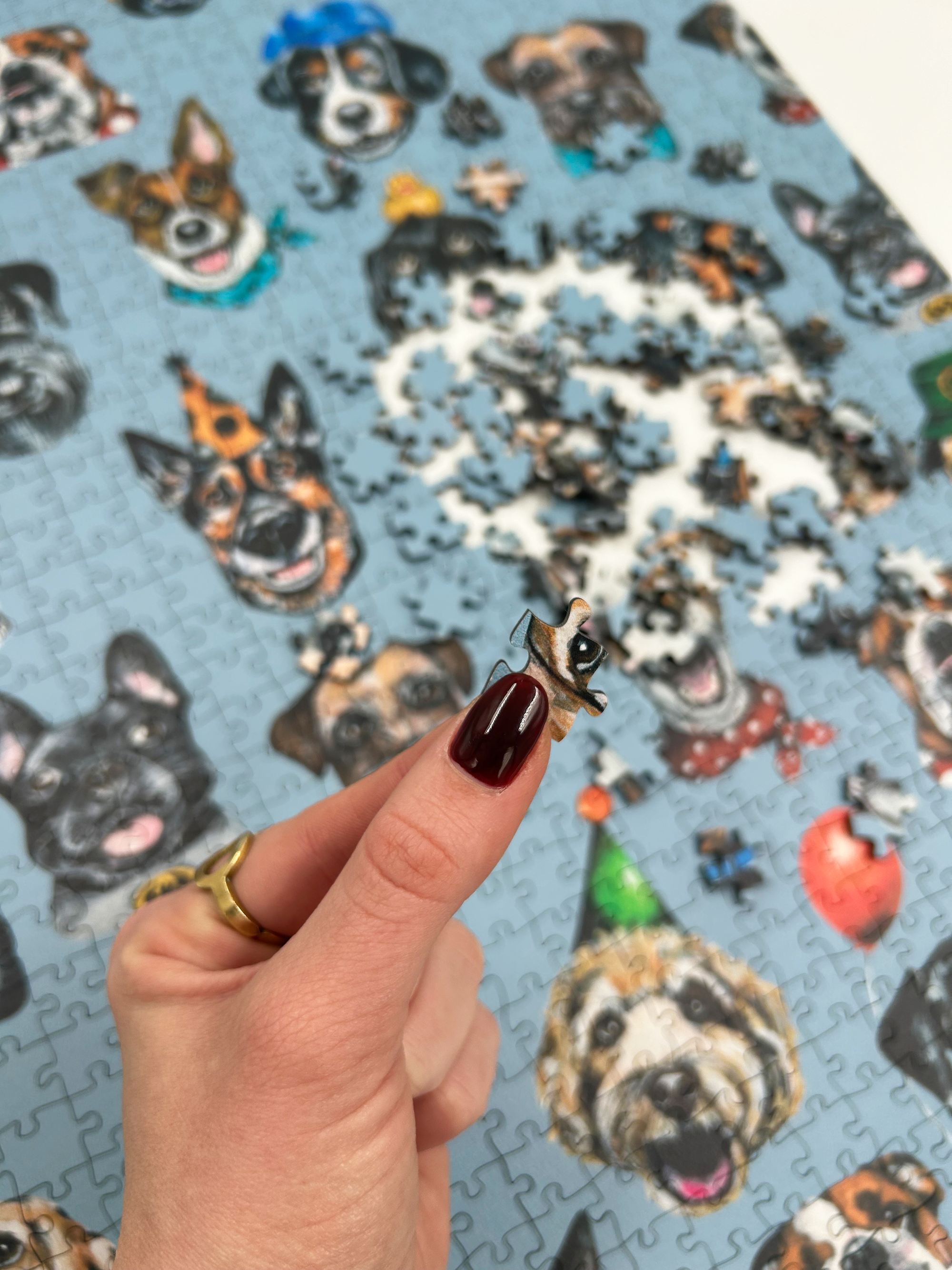 Hand holding a puzzle piece in front of a partially completed puzzle with dog illustrations on a blue background.