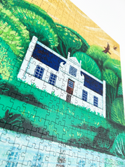 A wooden jigsaw puzzle featuring an illustration of the Zevenwacht Wine Estate manor house. Perfect for art lovers and anyone looking for a thoughtful gift. 