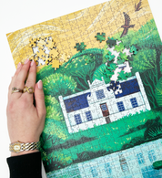 A wooden jigsaw puzzle featuring an illustration of the Zevenwacht Wine Estate manor house. Perfect for art lovers and anyone looking for a thoughtful gift. 